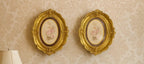 A pair of vintage-style oval frames in a richly gilded finish, each with a delicate floral cente...